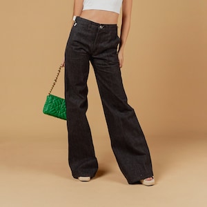 May include: A white halter top and dark denim wide-leg trousers are the focus of this fashion image. A green quilted handbag with a gold chain strap adds a splash of colour. The outfit is completed with white sandals.