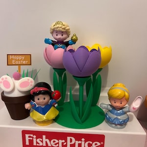 May include: A Fisher-Price toy set with Disney princess figurines and Easter decorations. The set includes Snow White with an apple, Cinderella with a shoe, and a princess in a flower. A sign reads "Happy Easter".