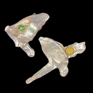 Puede incluir: Un par de pendientes de perla blanca con piedras preciosas verdes y amarillas. Los pendientes tienen una forma irregular y un aspecto natural y orgánico.