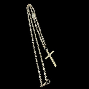 May include: A silver chain necklace with a small cross pendant. The chain is double-stranded and has a small pearl-like bead at the top.