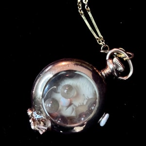 May include: A silver pocket watch with a chain, featuring a white cameo inside a glass dome surrounded by small pearls.