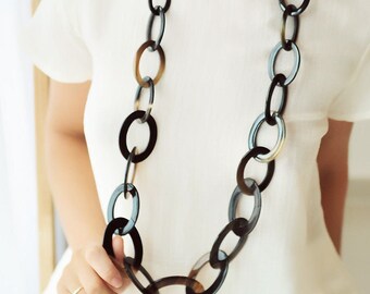 Peut inclure: Un long collier composé de gros maillons ovales en corne noire et brune.