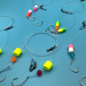 May include: A set of six fishing rigs with different colored beads and floats. Each rig has a hook and a swivel. The rigs are designed for catching fish.