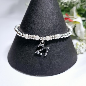Op de afbeelding: Zilveren armband met kralen en een zilveren bedel met de tekst "21".