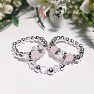 May include: Three beaded rings featuring metallic silver-toned spheres, clear ribbed glass beads, and smooth pale pink round stones. Each ring is constructed with a repeating pattern of these beads, creating a circular band design.