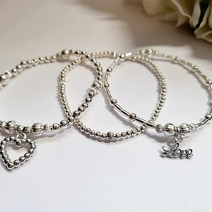 Peut inclure: Trois bracelets en argent perlé avec des breloques. Un bracelet a un charme en forme de cœur, et l'autre a un charme qui dit "Love".