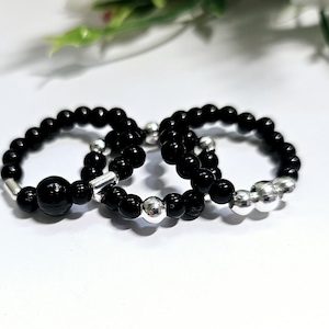 May include: Three black beaded rings with silver beads. The rings are stacked on top of each other.