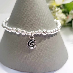 Könnte beinhalten: Ein silbernes Armband mit Perlen und einem Anhänger in Form einer Spirale.
