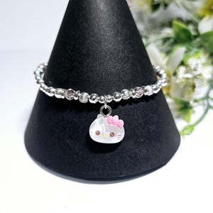 Puede incluir: Un brazalete de plata con un dije de Hello Kitty. El brazalete está hecho de pequeñas cuentas de plata y tiene un dije de Hello Kitty rosa con un lazo rosa.