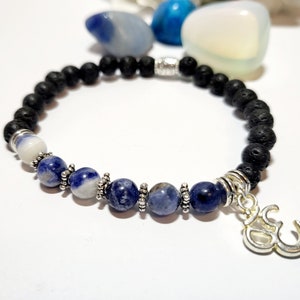 Può includere: Un braccialetto in pietra lavica nera con perline di sodalite blu e bianche e un ciondolo Om argentato.