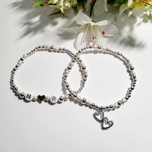 May include: Two silver beaded bracelets with a heart charm and letter beads spelling "NR".