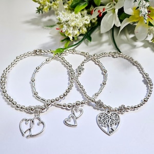 May include: Three silver bracelets with charms. The charms are a double heart, a single heart, and a tree of life design.