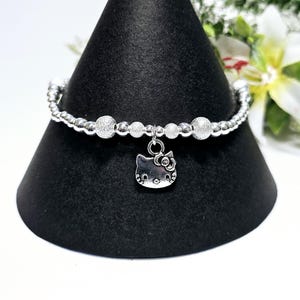 Puede incluir: Un brazalete de plata con un dije de Hello Kitty. El brazalete está hecho de pequeñas cuentas de plata con un acabado brillante.