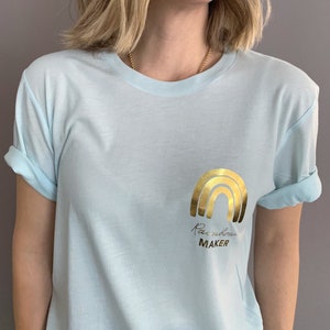 May include: A light blue t-shirt with a gold foil rainbow and the text "Rainbow Maker" on the front.