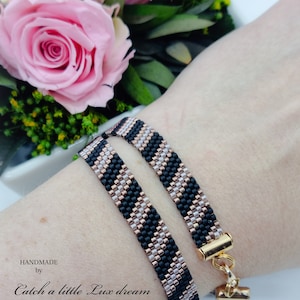 Puede incluir: Dos pulseras de cuentas negras y oro rosa con un cierre dorado. Las pulseras están superpuestas en la muñeca de una persona. El texto "HANDMADE by Catch a little Lux dream" es visible en la muñeca.