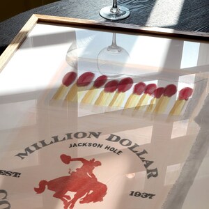 May include: A framed print of a vintage poster for the Million Dollar Cowboy Bar in Jackson Hole, Wyoming. The poster features a red cowboy riding a bucking horse with the text "Million Dollar Cowboy Bar" and "Jackson Hole, Wyoming, Est. 1937".