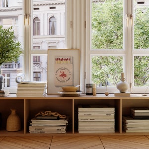 May include: A wooden shelf unit with a framed print of a red bull riding a cowboy on a box of matches. The print reads "Million Dollar Cowboy Bar". The shelf is decorated with a bowl, a vase, a candle, and a stack of magazines.