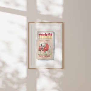 May include: A watercolor illustration of a matchbox with a white bulldog wearing a red and black jersey with the text "University of Georgia". The matchbox is labeled "University of Georgia" and "Georgia".