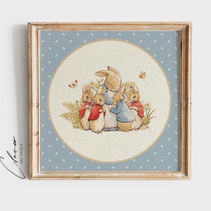 Puede incluir: Una impresión enmarcada con una ilustración en acuarela de una familia de conejos. Los conejos están rodeados de flores y mariposas, sobre un fondo azul claro con lunares blancos. El marco es de color marrón claro.