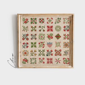 Op de afbeelding: Een ingelijste print met een verzameling kleurrijke bloemen- en geometrische quiltblokontwerpen. De blokken zijn rood, groen en crème, gerangschikt in een rasterpatroon. De lichte houten lijst voegt een rustieke toets toe aan het kunstwerk.