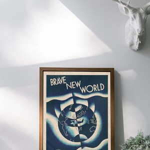 May include: A framed print of "Brave New World" by Aldous Huxley. The artwork features a blue and white design with a world map at the centre. The print is in a brown wooden frame and is displayed on a white wall.