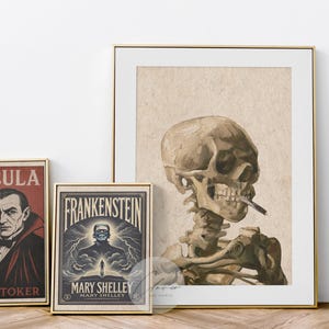 May include: A collection of framed art prints with a horror theme. The prints include a Dracula poster by Bram Stoker, a Frankenstein poster by Mary Shelley, and a skeleton smoking a cigarette. All prints are in gold frames.