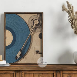 May include: A framed print of a vintage record player with a blue vinyl record. The artwork is displayed on a wooden cabinet, with a white vase holding dried plants to the right. A white mug and books are on the cabinet.