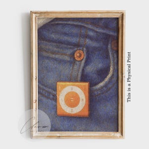 Puede incluir: Obra de arte enmarcada que presenta un primer plano de unos vaqueros azules con un bolsillo y un pequeño reproductor de MP3 naranja y blanco. La obra está en un marco de madera y tiene el texto "This is a Physical Print".