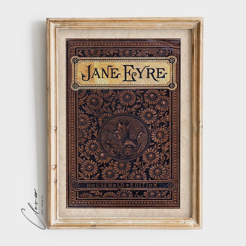 May include: A framed print of the book cover for "Jane Eyre: Household Edition". The cover features a brown leather-like background with a gold embossed title and a floral design. A butterfly is depicted in the center of the design.