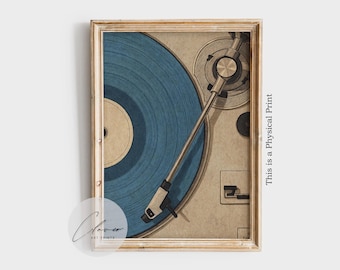 May include: Framed print of a vintage record player with a blue vinyl record. The artwork has a retro aesthetic, with a light brown background and a wooden frame. The text "This is a Physical Print" is visible.
