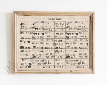 May include: A framed vintage-style calendar with a black and white design. The calendar has a date due column and dates listed in a grid format. The dates are printed in black ink and include months and years. The calendar is framed in a light wood frame.
