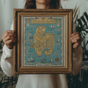 May include: A person holding a framed map of Treasure Island. The map is in a gold frame and has a blue background with a yellow island in the center. The map is surrounded by a white border.
