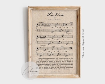 May include: Framed print of sheet music for "Für Elise" by Ludwig van Beethoven. The print features musical notes and text on aged paper, set within a light brown wooden frame. The text "This is a Physical Print" is printed vertically on the right side.
