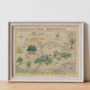 May include: Framed map of The Hundred Acre Woods from Winnie-the-Pooh, featuring a hand-drawn style with whimsical illustrations of locations like Rabbit's House and Pooh's house. The map is in a white frame, resting on a wooden surface.