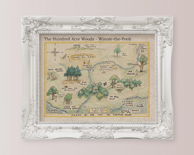 May include: A framed print of a map of the Hundred Acre Woods from Winnie-the-Pooh. The map is hand-drawn with watercolor-style illustrations and text. The white frame has ornate detailing.