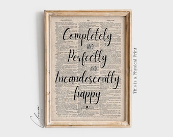 May include: A framed print with the words "Completely and Perfectly and Incandescently happy" in black script on a vintage dictionary page. The frame is light brown.