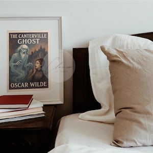 May include: A framed print of "The Canterville Ghost" by Oscar Wilde, with a ghostly figure and a woman in a vintage style. The print is on a nightstand with books, next to a bed with pillows and a white duvet. The frame is white.