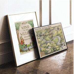 May include: Two framed prints leaning against a wall. One features the book cover of "Wind in the Willows" by Kenneth Grahame, with illustrations. The other is a map titled "River Bank - Wind in the Willows", with a compass rose.