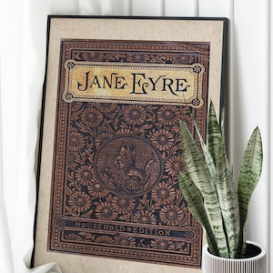 May include: A framed print of the book cover for "Jane Eyre" with a decorative floral design and the text "Household Edition".