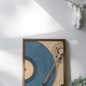May include: A framed print of a vintage record player with a blue vinyl record. The artwork has a retro aesthetic, with a brown wooden frame. A white deer head sculpture is mounted on the wall above the print.