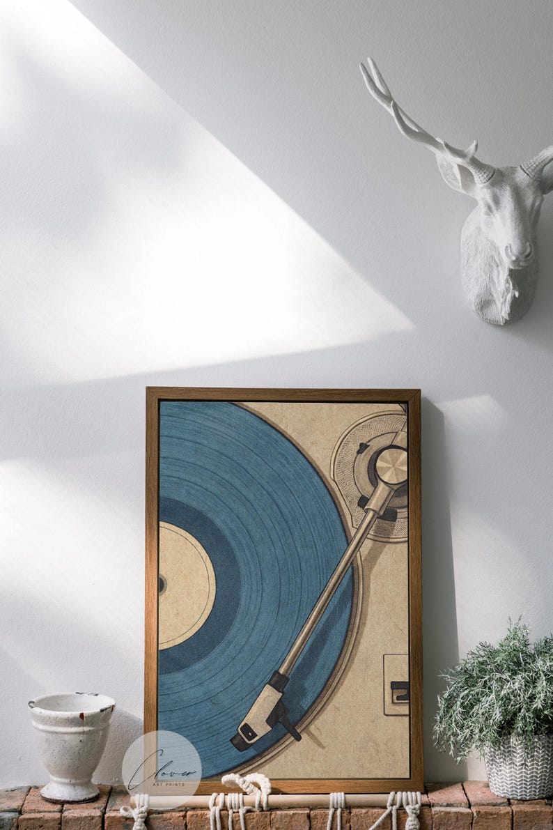 May include: A framed print of a vintage record player with a blue vinyl record. The artwork has a retro aesthetic, with a brown wooden frame. A white deer head sculpture is mounted on the wall above the print.
