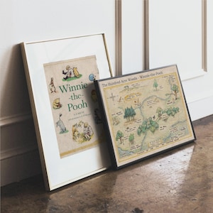 May include: Two framed prints featuring Winnie-the-Pooh. One is a book cover with illustrations and the title "Winnie-the-Pooh." The other is a map of the Hundred Acre Wood, with trees, rivers, and landmarks. Both are in neutral-toned frames.