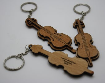 Puede incluir: Tres llaveros de madera en forma de violonchelo con anillas de plata. Los llaveros están grabados con el texto "Laura Hopkins Orchestra 2022".