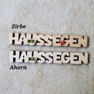 May include: Two wooden signs with the German word "Haus Segen" (House Blessing) spelled out in individual letters. The top sign is made of Zirbe wood and the bottom sign is made of Ahorn wood.