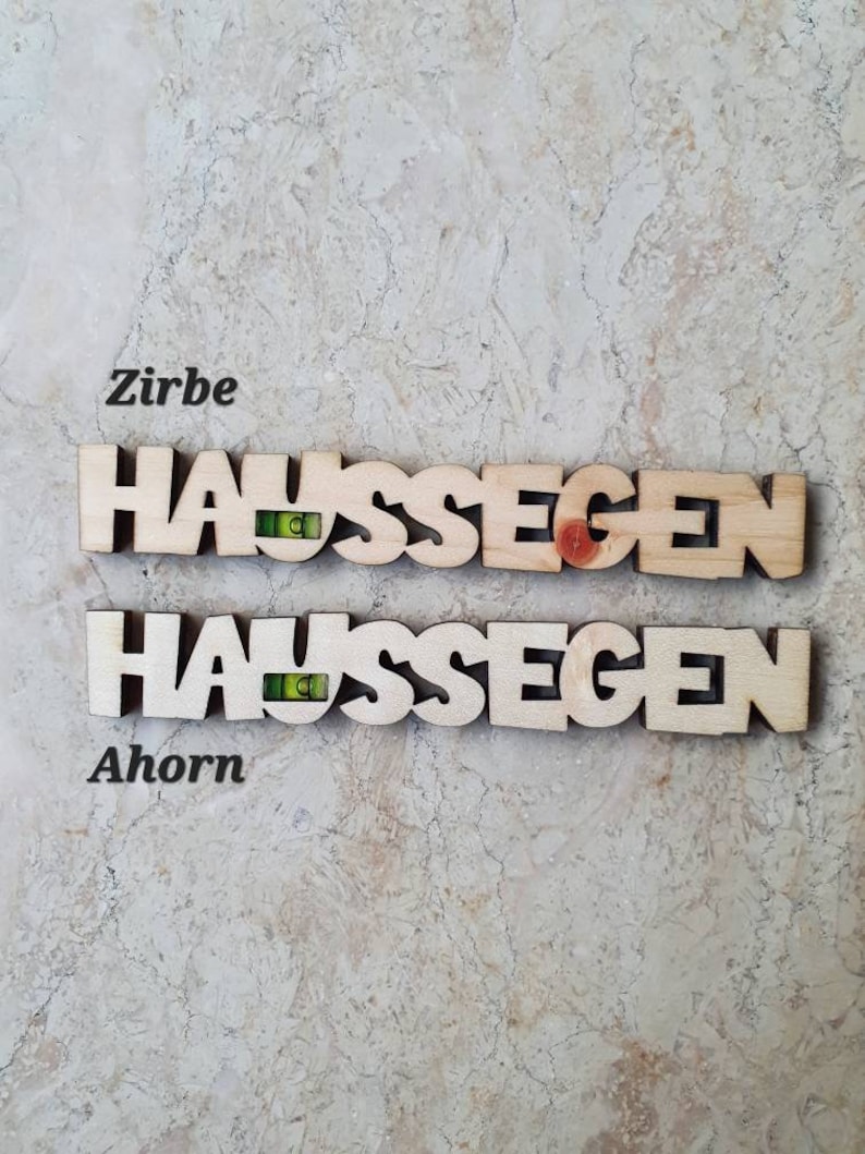 May include: Two wooden signs with the German word "Haus Segen" (House Blessing) spelled out in individual letters. The top sign is made of Zirbe wood and the bottom sign is made of Ahorn wood.