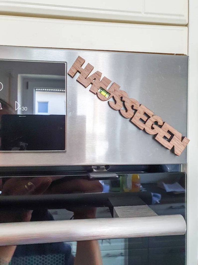 May include: A wooden sign with the word "Haussegen" in German, meaning "blessing of the house", is attached to a stainless steel oven door.