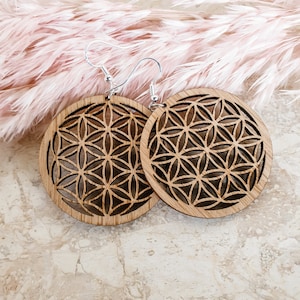 May include: A pair of wooden earrings featuring a flower of life design. The earrings are round and have a silver hook.