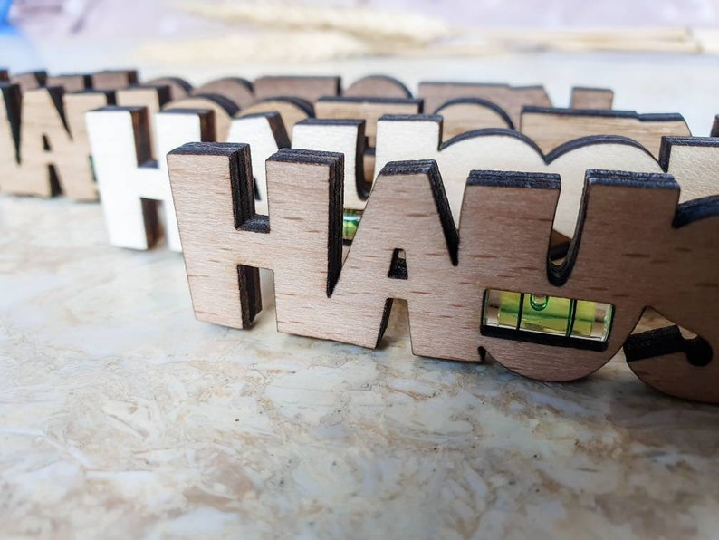 May include: A close-up of a wooden sign spelling "HAUS" with a small level embedded in the "U". The sign is made of light brown wood with dark brown edges.