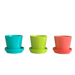 May include: Three colorful plastic plant pots with matching saucers. The pots are turquoise, green, and orange.