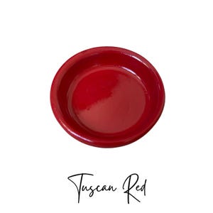 May include: A small, round, red ceramic dish. The dish is glazed and has a smooth, shiny finish. The text "Tuscan Red" is written below the dish.